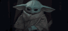 a baby yoda is sitting in a chair and holding a lightsaber .