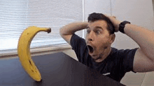 a man is sitting at a table with his mouth open while a banana is sitting on the table .
