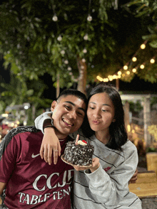 a man wearing a maroon ccj table ten shirt holds a cake
