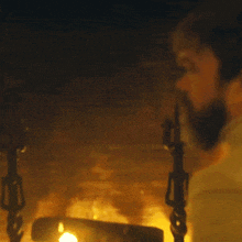 a man with a beard is standing in front of a fireplace in a dark room .