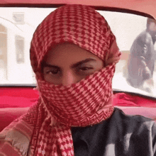 a man wearing a red scarf covering his face is sitting in a car