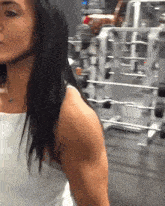 a woman is lifting dumbbells in a gym while wearing a white tank top