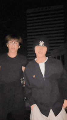 a man wearing a ny hat stands next to another man wearing a black jacket