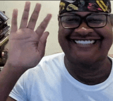 a man with glasses and a bandana on his head is smiling and waving his hand .