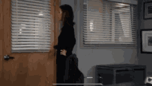 a woman stands in front of a window with blinds on it