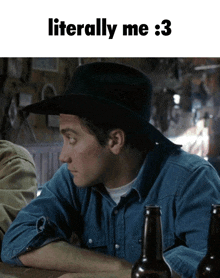 a man wearing a cowboy hat is sitting at a table with a bottle of beer