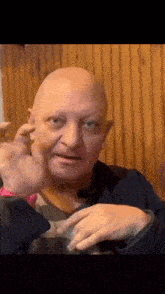 a bald man is making a funny face while sitting at a table in front of a wooden wall .