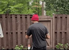 a man is standing in front of a wooden fence wearing a red hat .