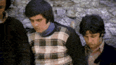 a man in a plaid sweater sits next to two other men