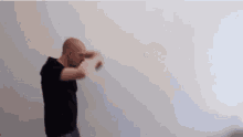 a bald man in a black shirt is standing in front of a white wall .