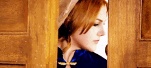 a woman wearing a blue cape and a hat is looking through a wooden door