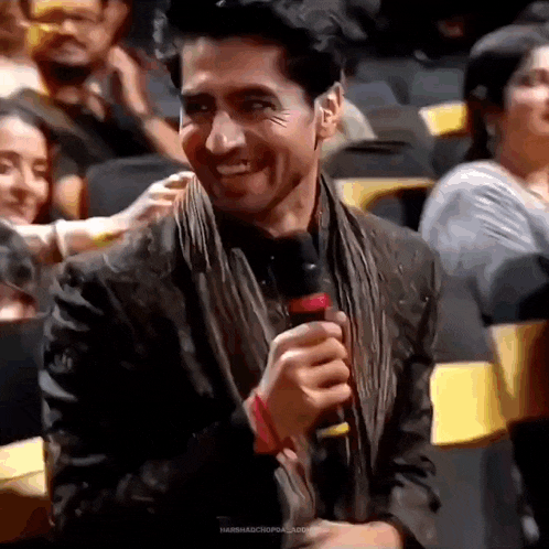 a man is holding a microphone and smiling while sitting in a theatre .