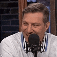 a man is smiling in front of a microphone while wearing a white shirt