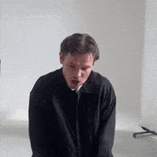 a man in a black jacket is sitting in a room