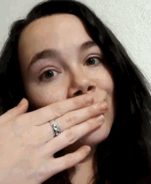 a woman with a ring on her finger covers her mouth with her hand