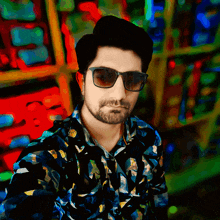 a man wearing sunglasses and a colorful shirt stands in front of a colorful background