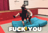 two men are wrestling on a blue mat with the words fuck you written above them