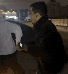 a man in a black jacket is standing next to a man in a white shirt