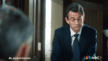 a man in a suit and tie is looking at himself in a mirror with a nbc logo behind him