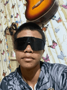 a man wearing sunglasses stands in front of a guitar on a wall with butterflies
