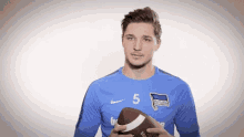 a man in a blue nike shirt is holding a football .