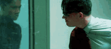 a man wearing glasses is looking at his reflection in a glass door .