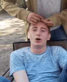 a man in a blue and white striped shirt is getting his hair done