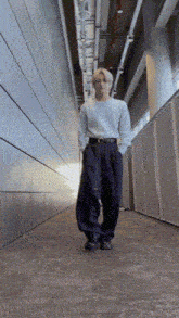 a man in a white sweater and blue pants is walking down a hallway