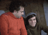 a man in a red sweater sits next to another man