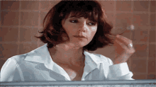 a woman in a white shirt looks at herself in a bathroom mirror