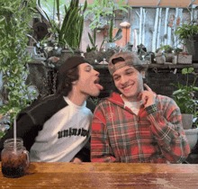two men are sitting at a table and one has a shirt that says unknow