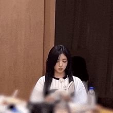 a woman with long black hair is sitting in a room with a bottle of water in front of her .