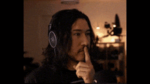 a man with long hair and a beard is wearing headphones and pointing at his ear .