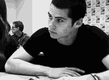 a black and white photo of a man sitting at a table with his hands on his lap .