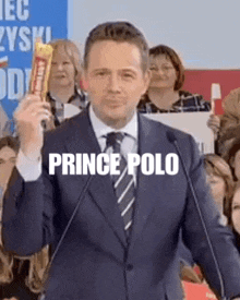a man in a suit and tie is holding a candy bar and giving a speech .