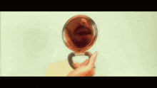 a woman is holding a round mirror with a ring on her finger