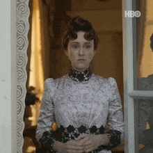 a woman in a pink and black dress is standing in front of a window with hbo written on the bottom