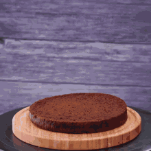 a person is spreading whipped cream on a chocolate cake on a wooden cutting board