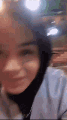 a close up of a woman 's face with a blurry background . she is wearing a hijab and smiling .