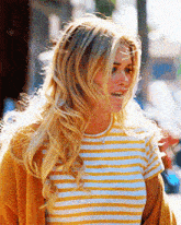 a woman wearing a yellow and white striped shirt is walking down the street