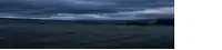a dark field with a cloudy sky and mountains in the background