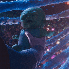a person is holding a green alien baby in their hands .