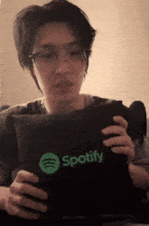 a man wearing glasses holds a spotify pillow in his hands