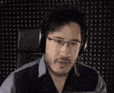 a man wearing headphones is sitting in front of a black wall and screaming .