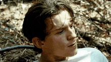 a young man is laying on the ground in the woods and looking at something .