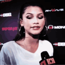 a woman wearing hoop earrings and a white shirt is talking into a microphone with the number 1 on it