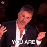 a man in a suit is holding a pair of glasses in front of a microphone and says " you are "