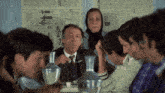 a group of people are sitting around a table with a sign on the wall that says ' t.c. '