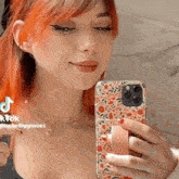 a woman with red hair is taking a selfie with her phone in a floral case .