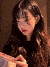 a girl with long hair and bangs is holding a box in her hands .